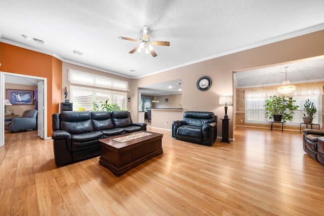 living area with ceiling fan, light wood-style flooring, healthy amount of natural light, crown molding, and a textured ceiling
