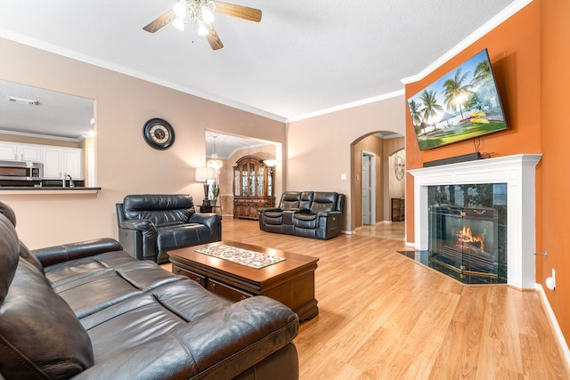 living room featuring arched walkways, wood finished floors, a ceiling fan, a fireplace, and crown molding
