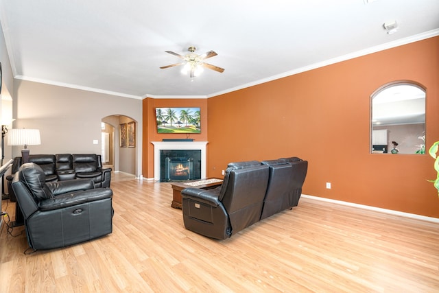 living room with arched walkways, a ceiling fan, light wood-style floors, crown molding, and baseboards