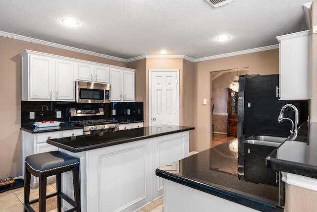 kitchen with appliances with stainless steel finishes, a sink, white cabinetry, dark countertops, and crown molding