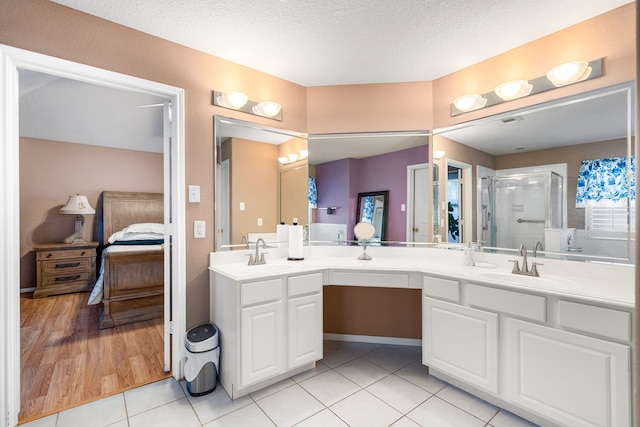 ensuite bathroom with double vanity, a shower stall, tile patterned floors, and a textured ceiling