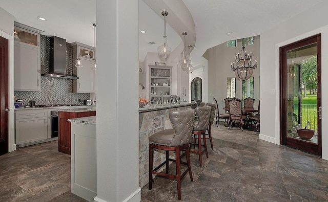 280 Sundog Rd, Huntsville, TX 77340 - kitchen featuring wall chimney range hood, a breakfast bar area, a chandelier, decorative backsplash, and baseboards