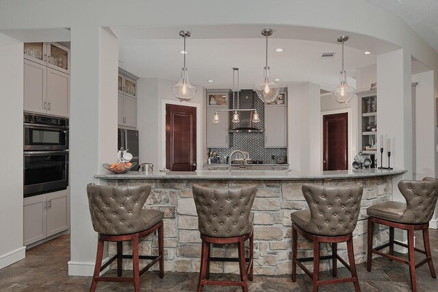 280 Sundog Rd, Huntsville, TX 77340 - kitchen with wall chimney exhaust hood, dark stone finish floors, a breakfast bar, tasteful backsplash, and a peninsula