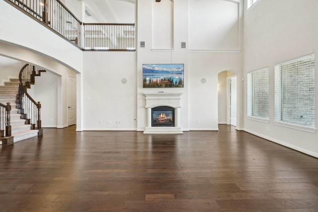 3115 Hillside Landing Trl, Katy, TX 77494 - unfurnished living room featuring arched walkways, a high ceiling, dark wood-style flooring, a glass covered fireplace, and stairs