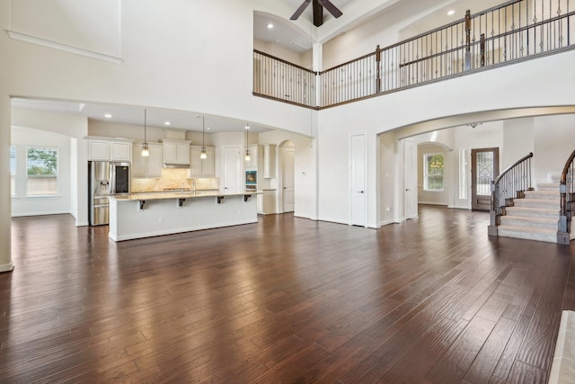 3115 Hillside Landing Trl, Katy, TX 77494 - unfurnished living room with arched walkways, a ceiling fan, dark wood-style floors, a high ceiling, and stairs