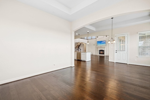 3115 Hillside Landing Trl, Katy, TX 77494 - unfurnished living room featuring arched walkways, dark wood-style flooring, baseboards, and a chandelier