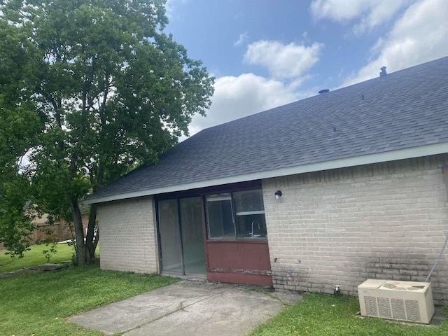 back of house featuring roof with shingles, brick siding, and a lawn