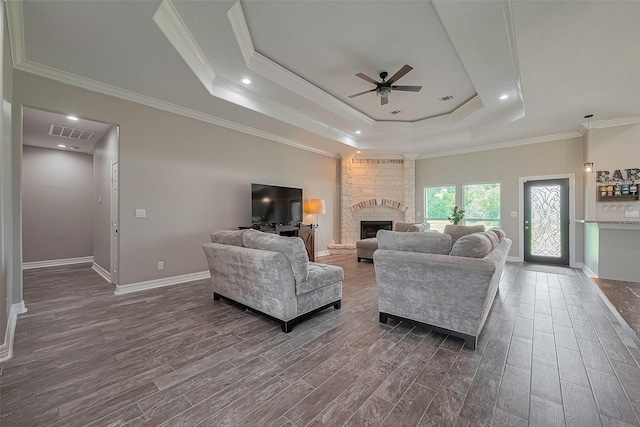 3331 Bridgette Ln, Baytown, TX 77523 - living room featuring a tray ceiling, dark wood-style flooring, a ceiling fan, a stone fireplace, and crown molding