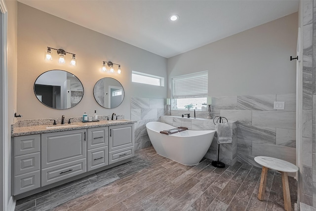 3331 Bridgette Ln, Baytown, TX 77523 - bathroom featuring tile walls, a soaking tub, double vanity, a wainscoted wall, and wood finished floors