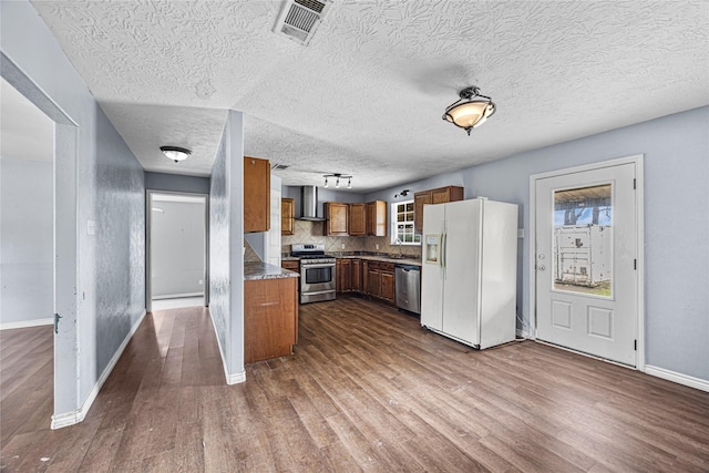 1826 Reese St, Liberty, TX 77575 - kitchen with appliances with stainless steel finishes, wall chimney exhaust hood, dark wood-style floors, brown cabinets, and a textured ceiling