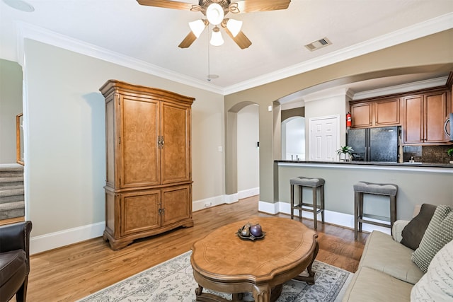 living room with a ceiling fan, light wood finished floors, arched walkways, baseboards, and ornamental molding