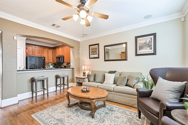 living area with ceiling fan, ornamental molding, light wood-type flooring, arched walkways, and baseboards