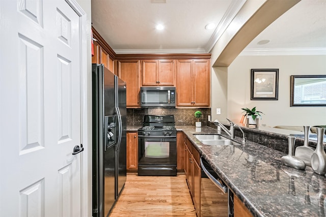 kitchen featuring black appliances, a sink, crown molding, light wood-style floors, and dark stone counters