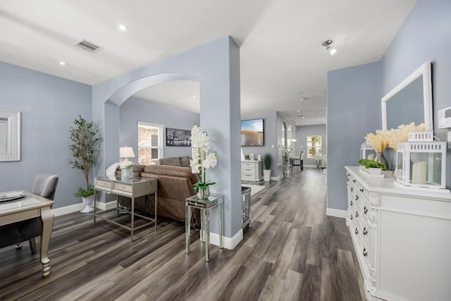 hall featuring dark wood finished floors, arched walkways, baseboards, recessed lighting, and a desk