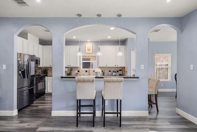 kitchen featuring stainless steel appliances, a kitchen bar, dark countertops, dark wood-style flooring, and recessed lighting