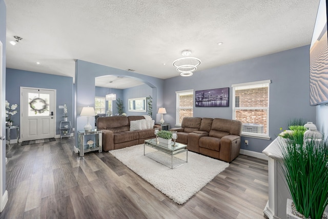 living area with arched walkways, baseboards, wood finished floors, plenty of natural light, and a textured ceiling