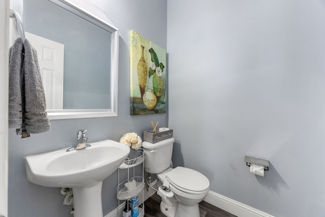 bathroom featuring toilet, baseboards, wood finished floors, and a sink