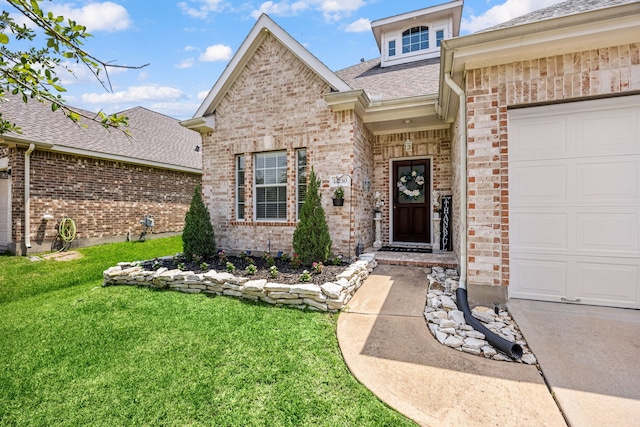entrance to property with brick siding, a lawn, roof with shingles, and a garage