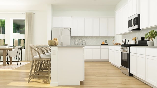 kitchen featuring white microwave, gas range, light wood-type flooring, backsplash, and white cabinets