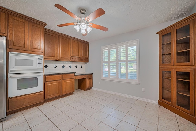 22010 Elsinore Dr, Katy, TX 77450 - kitchen featuring white appliances, brown cabinetry, a textured ceiling, light tile patterned flooring, and glass insert cabinets