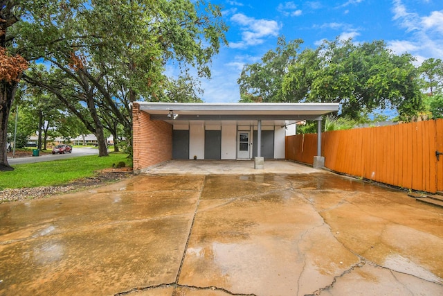 garage featuring driveway, fence, and a detached carport