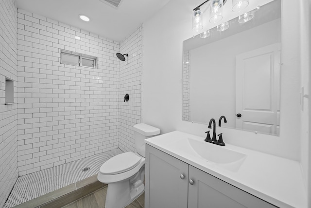 bathroom with toilet, a tile shower, vanity, and recessed lighting
