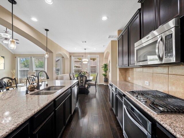 18118 Berry Garden Ln, Spring, TX 77379 - kitchen with stainless steel appliances, a sink, arched walkways, light stone counters, and dark wood-style floors