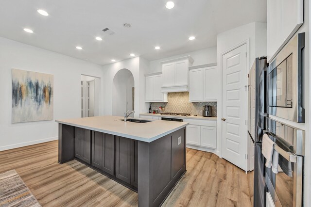 19015 Giara Pony Trl, Tomball, TX 77377 - kitchen featuring arched walkways, light wood-type flooring, stainless steel appliances, a center island with sink, and recessed lighting