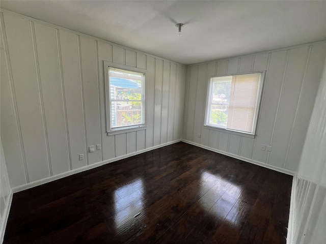 unfurnished room featuring a decorative wall, dark wood-style flooring, and baseboards
