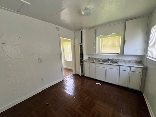 kitchen featuring a sink, baseboards, light countertops, and white cabinets