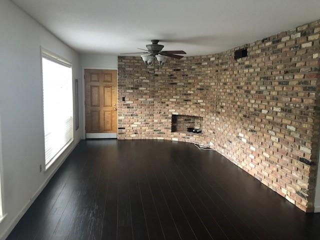 2101 Fountain View Dr Unit 77, Houston, TX 77057 - unfurnished living room featuring ceiling fan, brick wall, dark wood-style flooring, and baseboards