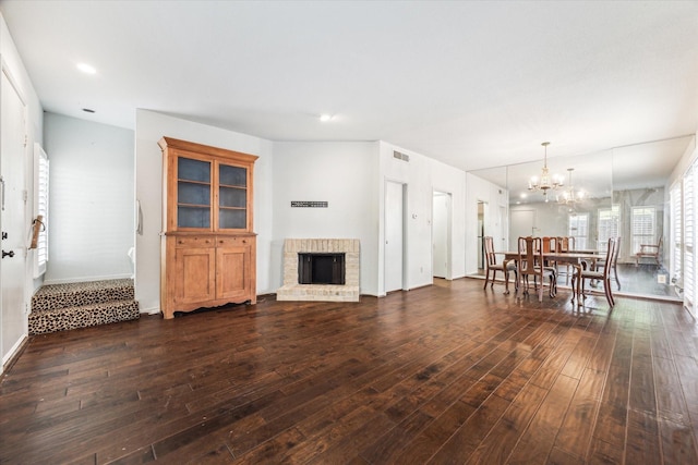 living room with hardwood / wood-style floors, a chandelier, a brick fireplace, and baseboards