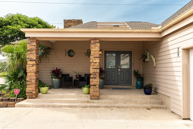 29 Quintana Dr, Galveston, TX 77554 - property entrance with roof with shingles, covered porch, and a chimney