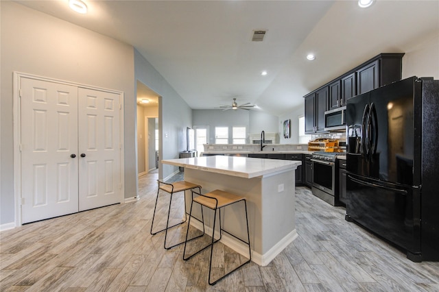 kitchen with appliances with stainless steel finishes, a breakfast bar area, a ceiling fan, light wood-type flooring, and dark cabinets