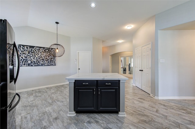 kitchen with stainless steel fridge, arched walkways, dark cabinets, hanging light fixtures, and light stone countertops