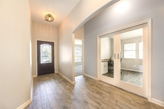 entryway with arched walkways, light wood-style flooring, french doors, and baseboards