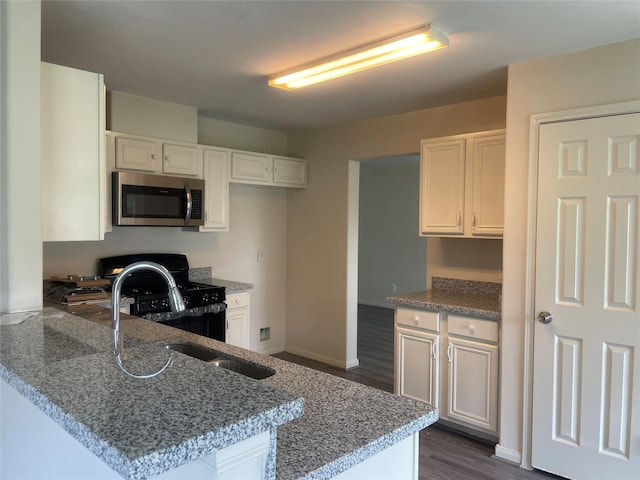 5918 Fergis Dr, Katy, TX 77449 - kitchen featuring stainless steel microwave, black range with gas stovetop, a peninsula, dark wood-style floors, and white cabinets