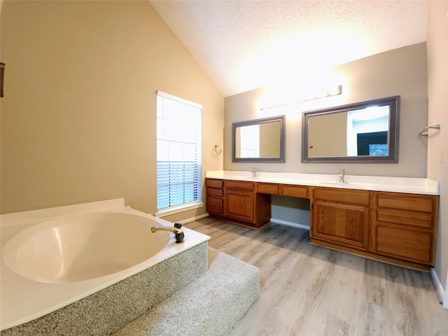 3226 Country Club Blvd, Stafford, TX 77477 - bathroom featuring lofted ceiling, double vanity, a bath, a textured ceiling, and wood finished floors