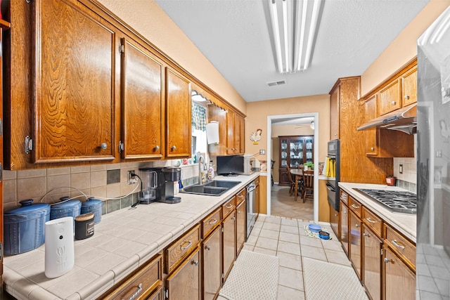 11855 23rd St, Santa Fe, TX 77510 - kitchen featuring appliances with stainless steel finishes, light tile patterned flooring, tile counters, a sink, and under cabinet range hood