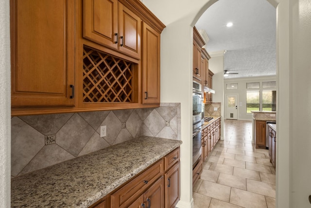 226 Beasley Reef Dr, Beach City, TX 77523 - kitchen featuring arched walkways, brown cabinetry, light stone counters, decorative backsplash, and stainless steel appliances