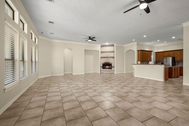 226 Beasley Reef Dr, Beach City, TX 77523 - unfurnished living room with a ceiling fan, a textured ceiling, arched walkways, a large fireplace, and crown molding