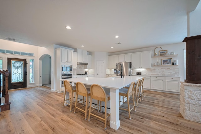 8113 Tranquil Lake Way, Conroe, TX 77385 - kitchen featuring appliances with stainless steel finishes, arched walkways, backsplash, light wood-style floors, and light countertops