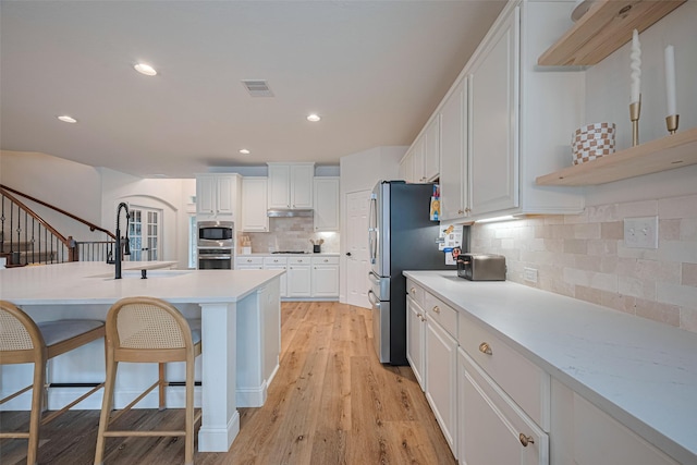 8113 Tranquil Lake Way, Conroe, TX 77385 - kitchen with stainless steel appliances, white cabinets, light countertops, decorative backsplash, and a breakfast bar area