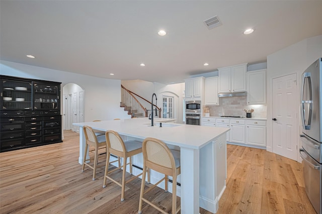8113 Tranquil Lake Way, Conroe, TX 77385 - kitchen with arched walkways, a sink, appliances with stainless steel finishes, under cabinet range hood, and white cabinetry