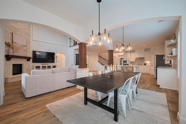 8113 Tranquil Lake Way, Conroe, TX 77385 - dining space featuring arched walkways, light wood-type flooring, stairs, ornate columns, and a chandelier