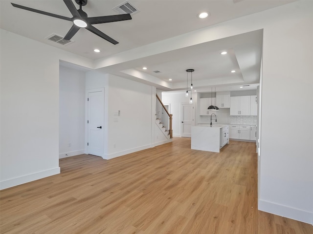 2207 Dan St, Houston, TX 77020 - unfurnished living room featuring a tray ceiling, stairs, a ceiling fan, light wood finished floors, and recessed lighting