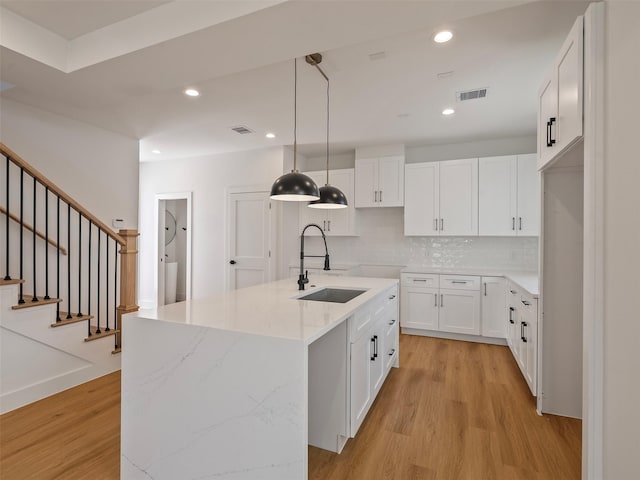 2207 Dan St, Houston, TX 77020 - kitchen featuring light wood finished floors, a kitchen island with sink, white cabinetry, backsplash, and light stone counters