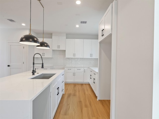 2207 Dan St, Houston, TX 77020 - kitchen with light wood-type flooring, white cabinetry, a center island with sink, recessed lighting, and tasteful backsplash