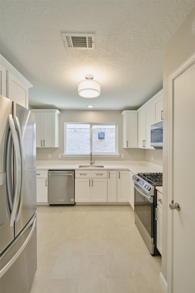 60 Hickory Oak Dr, The Woodlands, TX 77381 - kitchen featuring appliances with stainless steel finishes, a sink, white cabinets, light countertops, and a textured ceiling