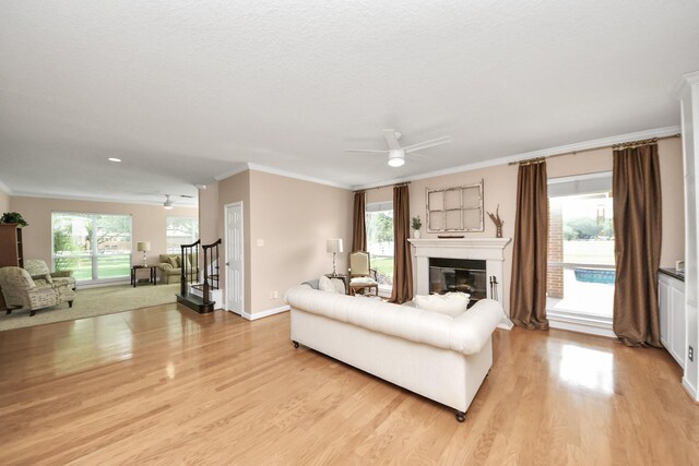 1140 Bartlett Rd, Katy, TX 77493 - living area featuring a glass covered fireplace, ornamental molding, light wood-style floors, stairway, and ceiling fan
